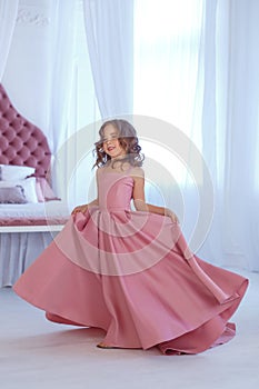 A small, beautiful girl in a luxurious pink dress, is gaily circling in a white room.