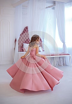 A small, beautiful girl in a luxurious pink dress, is gaily circling in a white room.