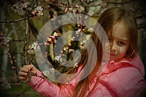 A small, beautiful girl in pink clothes walking in the Park near a flowering tree