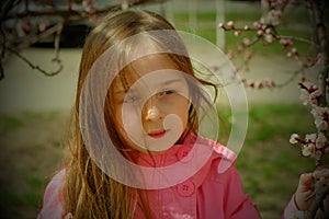 A small, beautiful girl in pink clothes walking in the Park near a flowering tree