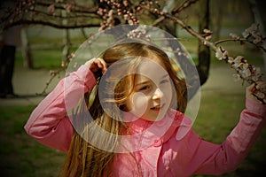 A small, beautiful girl in pink clothes walking in the Park near a flowering tree