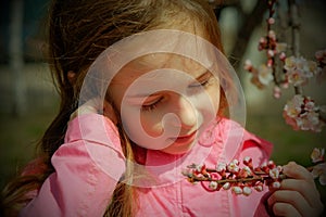 A small, beautiful girl in pink clothes walking in the Park near a flowering tree