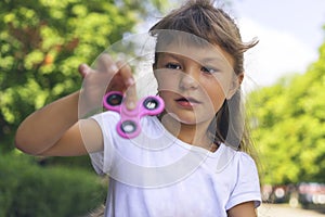 A small beautiful girl in a white T-shirt is disgusted and cautiously holding a pink spinner in her hand on the street