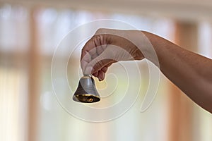 A small bell in a grandmother's hand against a neutral background in a room, close-up,