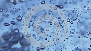 Small and big air bubbles in water rising in slow motion on blue background