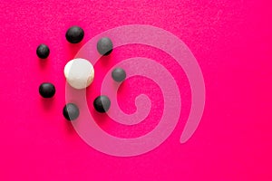 Small black balls surrounding a large white plasticine ball on pink vibrant background. Concepts of bullying and racism, social