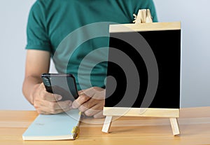 Small black board on wooden table,blank blackboard isolated and man used smartphone