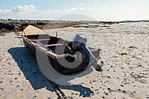 Small black color fishing motor boat on a sand at low tide. Fishing industry, Unique design with high bow. Warm sunny day