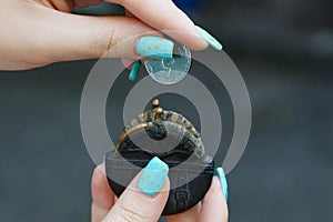 A small black open purse and a coin in the hands of a girl