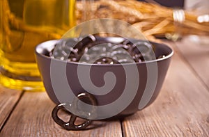 Small black pretzels in a bowl with glass ob beer on the wooden table