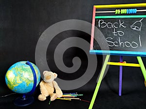 Small blackboard, color pencils and globe and teddybear on black. Back to school
