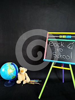 Small blackboard, color pencils and globe and teddybear on black. Back to school