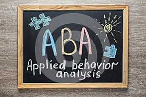 Small blackboard with text ABA Applied behavior analysis and drawings on wooden table, top view