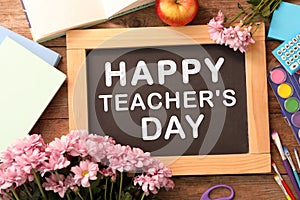 Small blackboard with text Happy Teacher`s Day, stationery and flowers on wooden table, top view