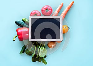 Small blackboard with vegetables around. Healthy concept on blue background with copy space.