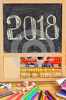 Small blackboard in wooden abacus frame and hand written 2018 new year greeting on it. Scattered stationery, colorful pencils, ch