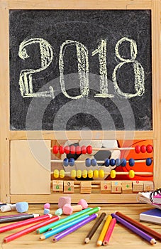 Small blackboard in wooden abacus frame and hand written 2018 new year greeting on it. Scattered stationery, colorful pencils, ch