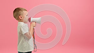 Small blond Caucasian boy in white T-shirt shouts loudly into white megaphone, place for text or advertising on pink