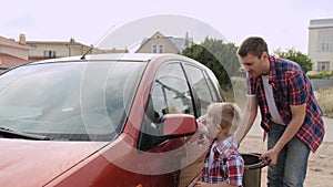 Small blond kid l washes the car`s headlight under the guardian of his young father slow motion