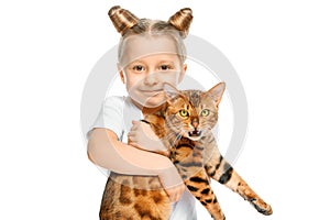 A small blonde girl holds a disgruntled Bengal cat in her hands on a white isolated background