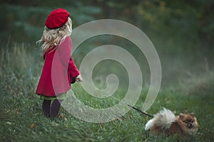 A small blonde with a small dog in the autumn misty forest looks into the distance. Autumn photography. Rear view