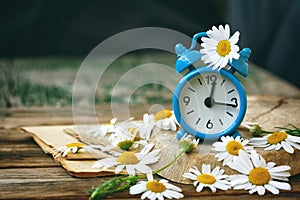 Small blue alarm clock and chamomile flowers on wooden table, summer time concept