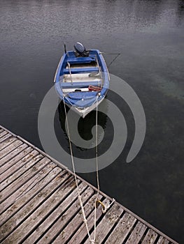 a small blue boat tied up to a wooden dock on a lake