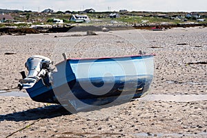 Small blue color fishing boat with red painted interior on a sandy beach at low tide. Food supply chain industry