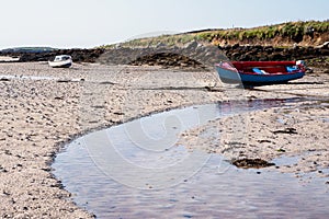 Small blue color fishing boat with red painted interior on a sandy beach at low tide. Food supply chain industry