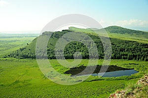 A small blue lake lying at the foot of a high gentle hill