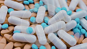 Small blue pills fall on white capsules with antibiotic and orange vitamins.