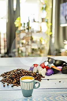 A small blue porcelain espresso cup on a table full of coffee beans and pods near the window