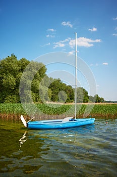 Small blue sailboat moored by reeds, Drawsko Lake, Poland