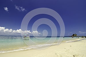 Small boat anchored with cloudy blue sky background and clear blue sea water.