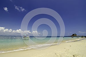 Small boat anchored with cloudy blue sky background and clear blue sea water.