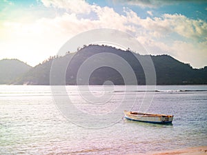 Small boat anchored off a Seychelles beach with light leak