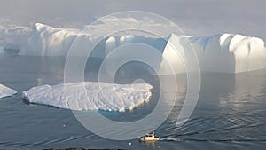 A small boat among icebergs in Disko Bay glacier during midnight sun Ilulissat, Greenland.