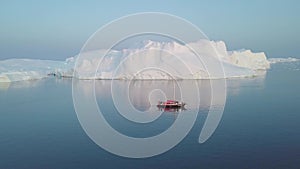 A small boat among icebergs in Disko Bay glacier during midnight sun Ilulissat, Greenland.