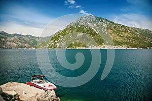 A small boat moored on the shore opposite the historic town of Perast at famous Bay of Kotor