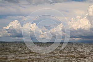 Small boat in ocean water with clear blue skies and large white clouds.