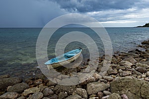 Small boat on rock beah with rain storm