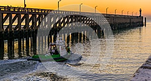 Small boat sailing in the harbor of Blankenberge, Belgium, view on the pier and lighthouse at sunset