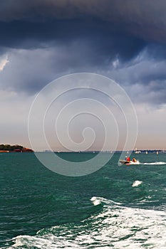 Small boat sailing past La Grazia or Santa Maria della Grazia island in Venetian lagoon in stormy weather with dark blue