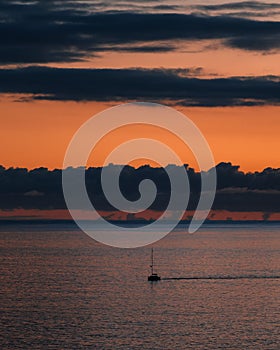Small boat silhouetted against the sky at twilight, drifting on the vast expanse of a tranquil lake.