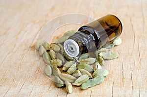 Small bottle with essential cardamon oil on the wooden background. Cardamom seeds close up. Aromatherapy, spa and herbal medicine