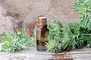 Small bottle with essential wormwood oil extract, tincture, infusion. Old wooden background. Aromatherapy, spa