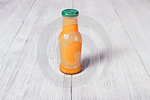 Small bottle of orange juice stands on white wooden table