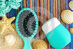 Small bottle with sunscreen lotion shampoo, conditioner and hairbrush on the colorful beach towel with sand and seashells.