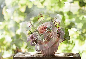 A small bouquet of autumn flowers in a pink mug on green natural outdoor background