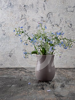 A small bouquet of blue forget-me-nots in a gray ceramic glass